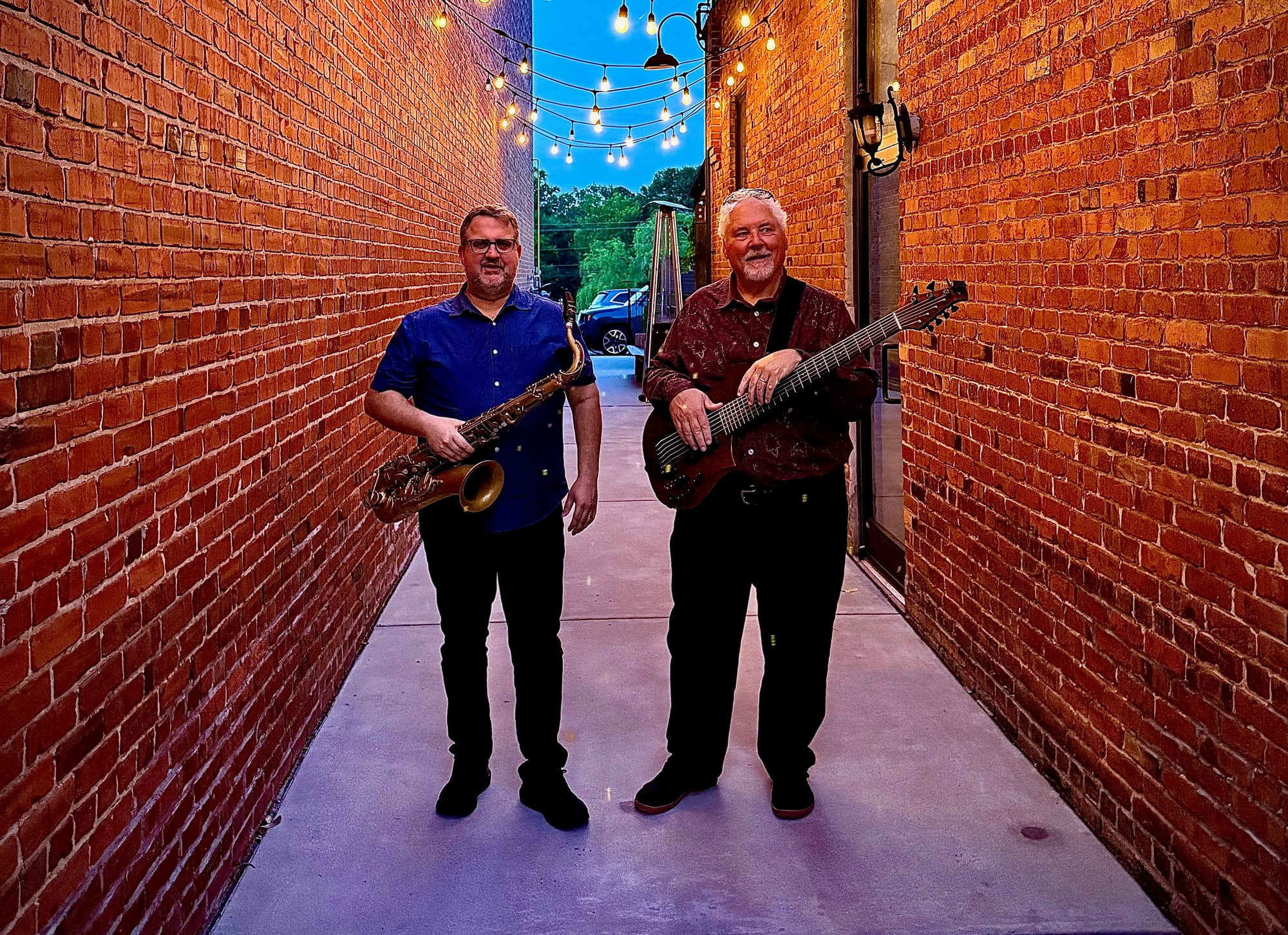 Rob Denty and Paul Westlake in a lantern-strung brick alley at dusk